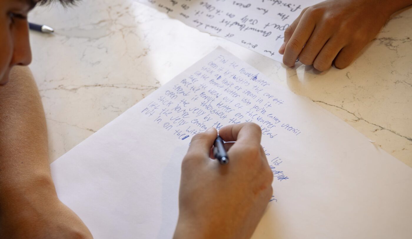 A participant handwrites step-by-step instructions during a Human Futures exercise